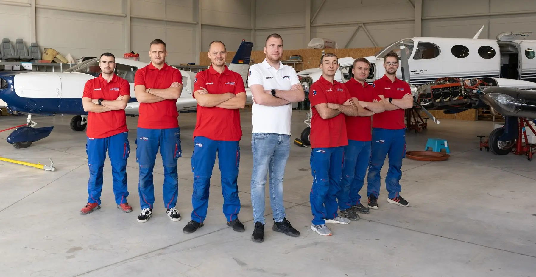 Seven members of the AIR TEAM hangar team standing in front of a Piper and a Cessna 340 in the hangar