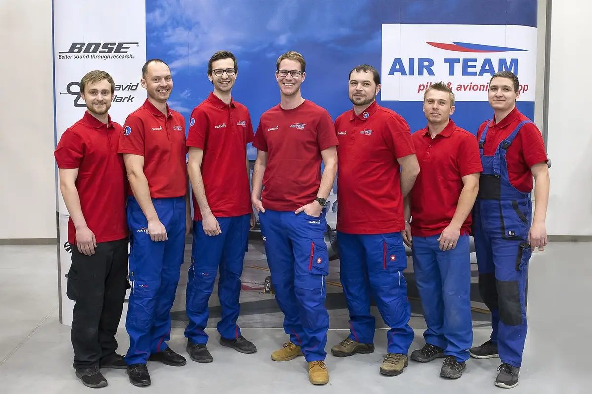 Seven AIR TEAM technicians in red polo shirts in front of a King Air