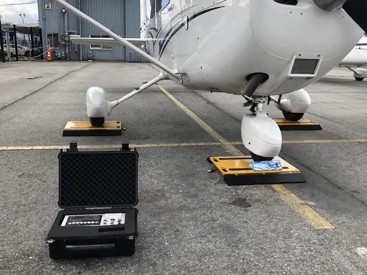 Weighing scales and a case with a readout beside a light aircraft