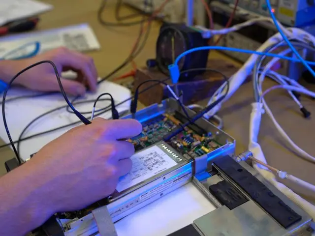 Hands testing a circuit board connected to a test set on a workbench