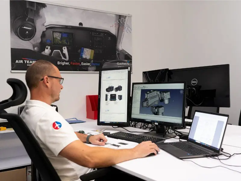Engineer reviewing certification documents at a desk with two monitors