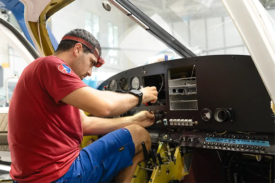 AIR TEAM avionics technician working behind an aircraft instrument panel in the hangar