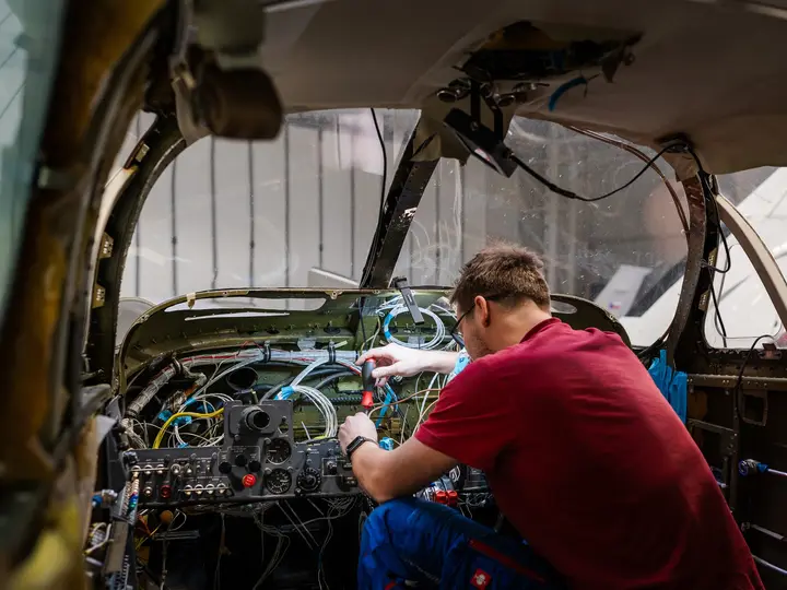 Technician working behind an open instrument panel with the wiring exposed
