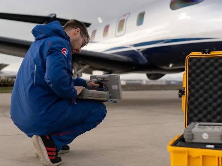 Technician operating a NAV/COMM/transponder tester from a yellow case beside an aircraft